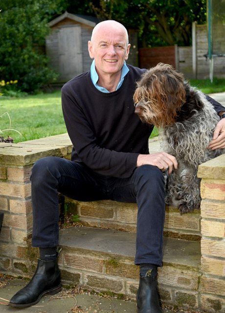 Andrew Devic smiling, sitting on a garden step with a shaggy dog