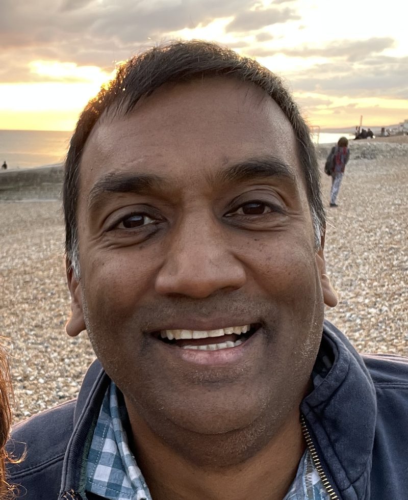 Bimbi Fernando smiling on a pebble beach at sunset